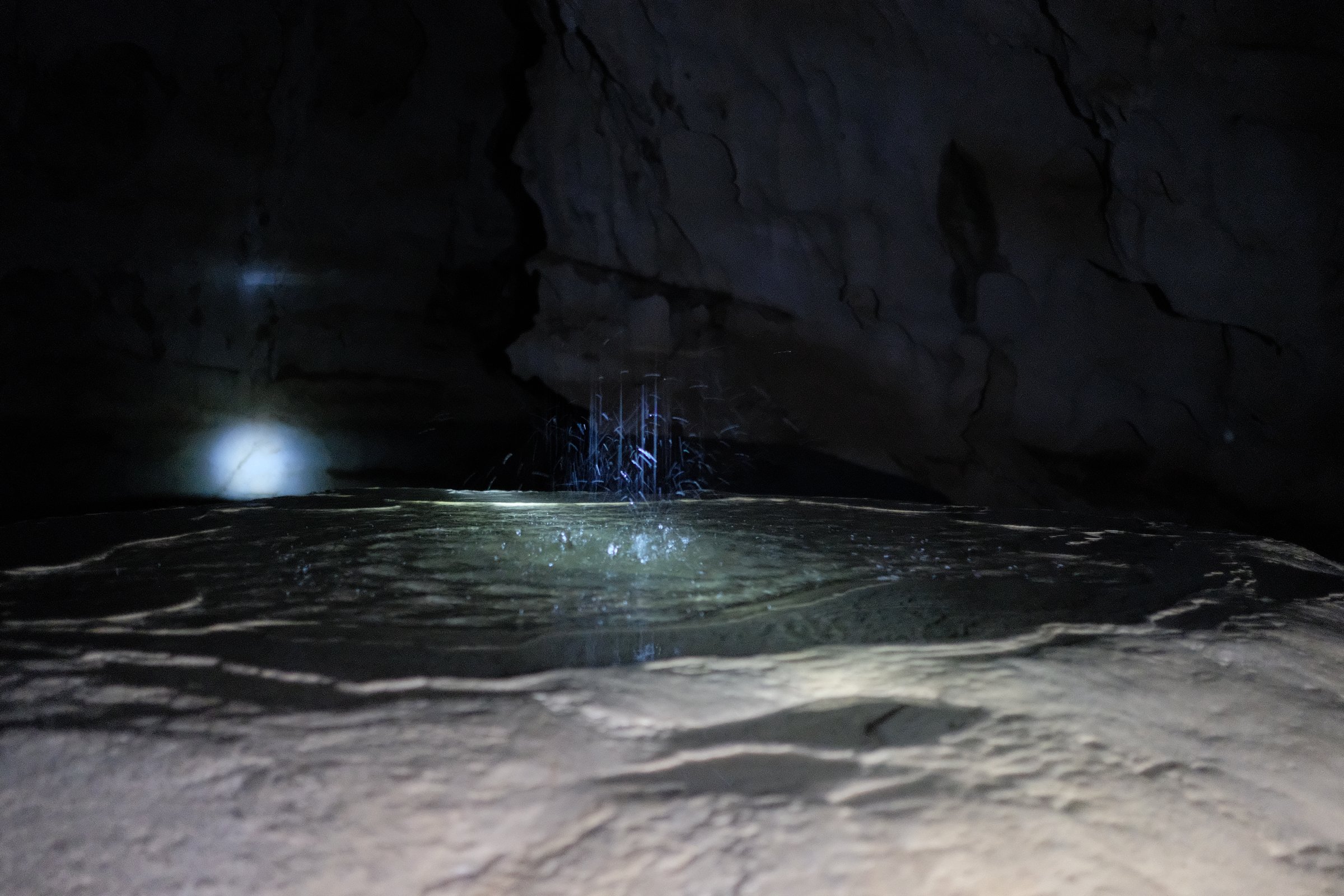 A small pool inside a cave, a thin stream falling above