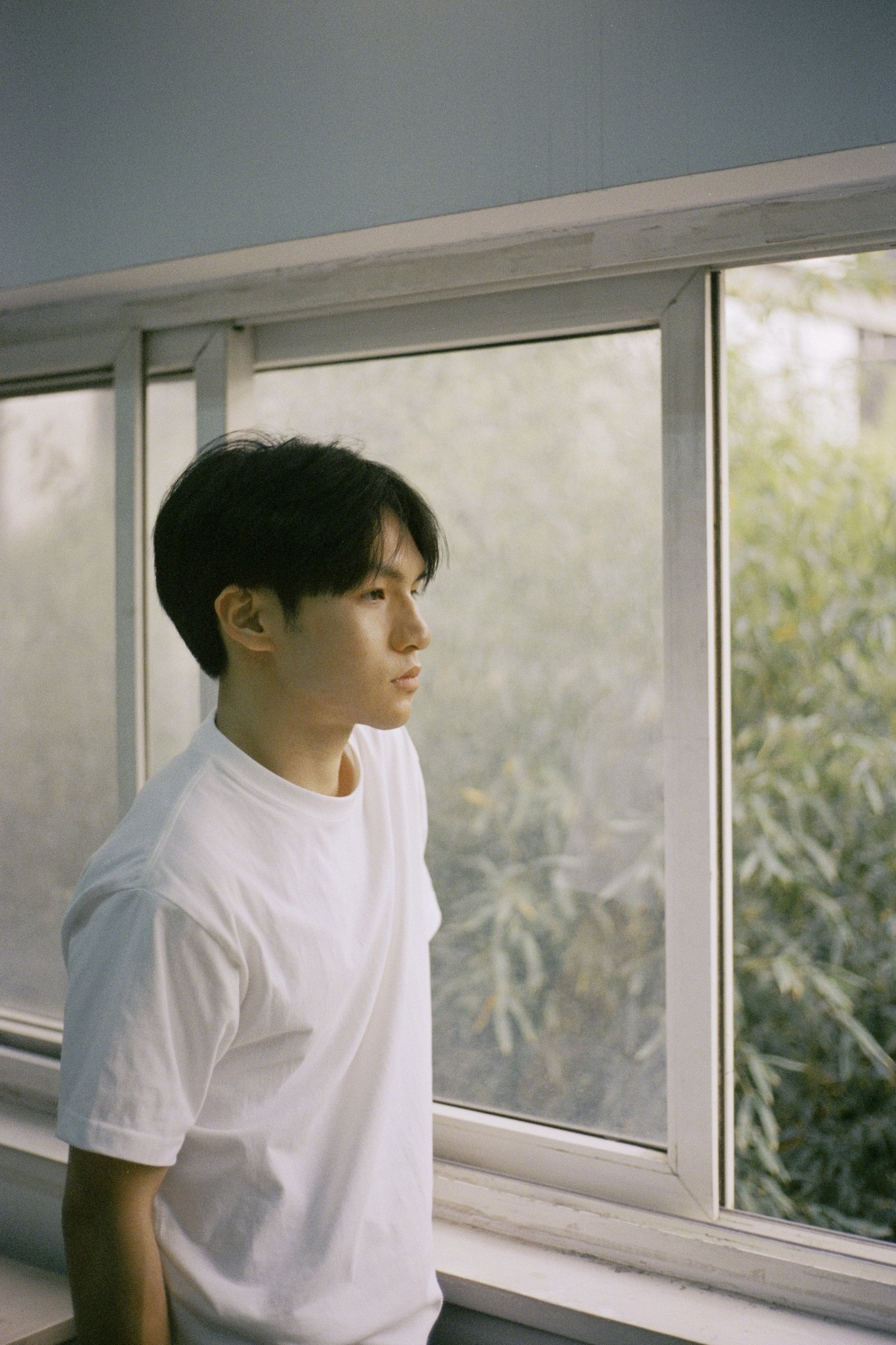 A young man by a window, white T-shirt, pale curtains